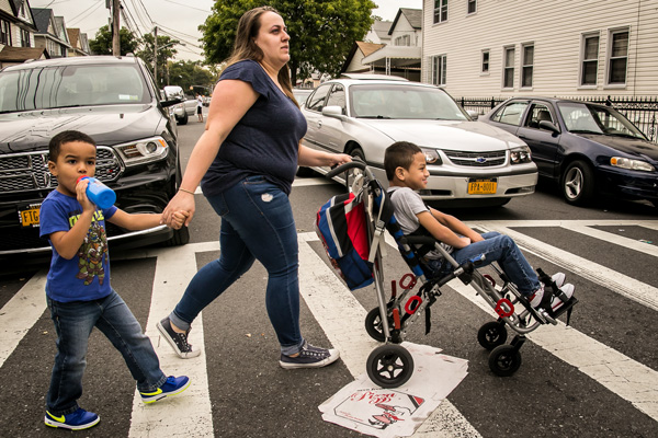 Lorraine Doucette crossing the street with her sons Liam (4 years old, walking) and Jason (6 years old, in the chair) on their way to pick up her daughters from school, a few block away from their home. Lorraine struggled to get Jason's public school to provide the services he needs.