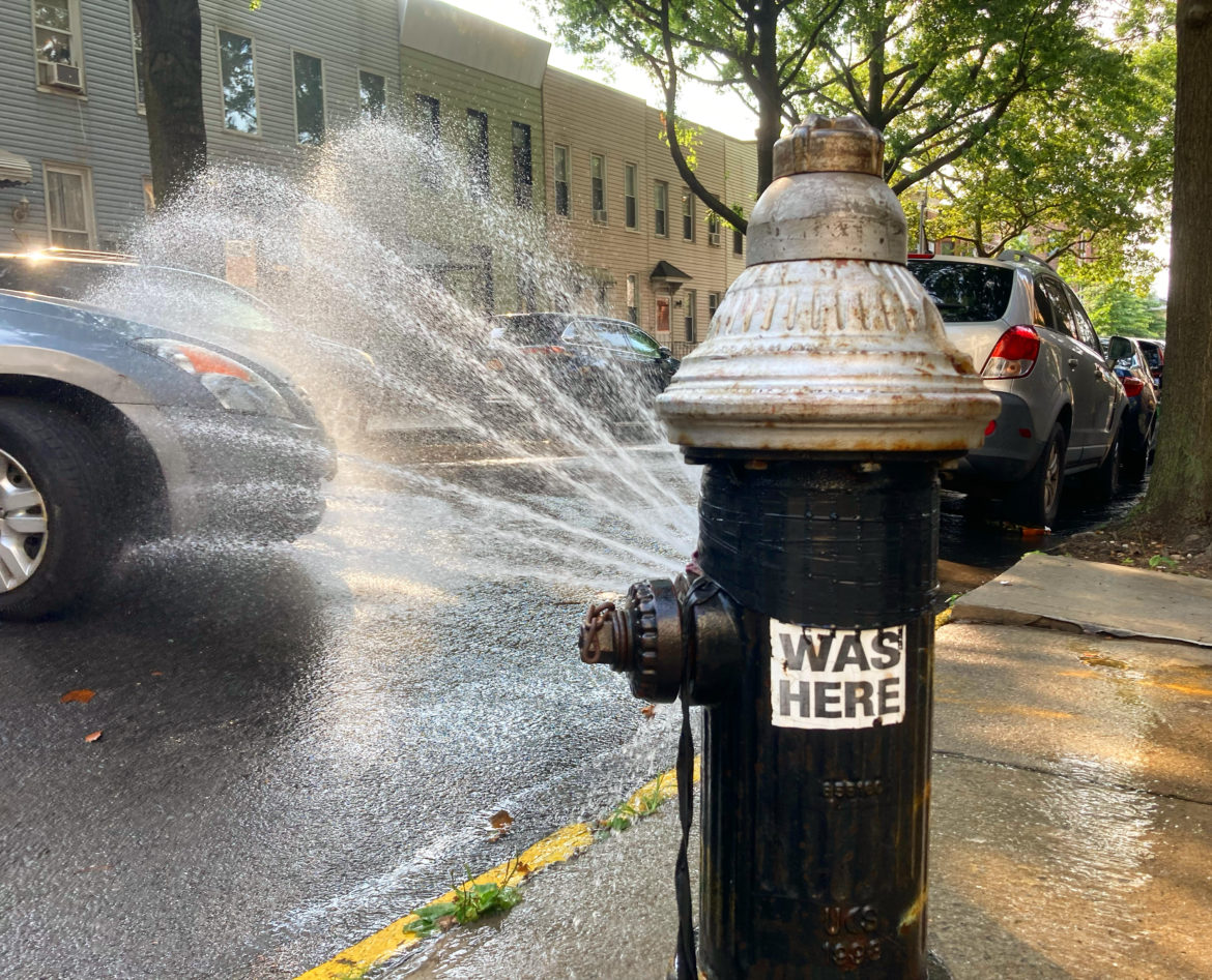 An open fire hydrant spraying water on a Brooklyn street