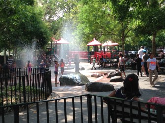 Children of Rayito De Luz Daycare cool off in the sprays of St. James Playground’s water spouts after getting permission from caretaker Daniel Pena. 