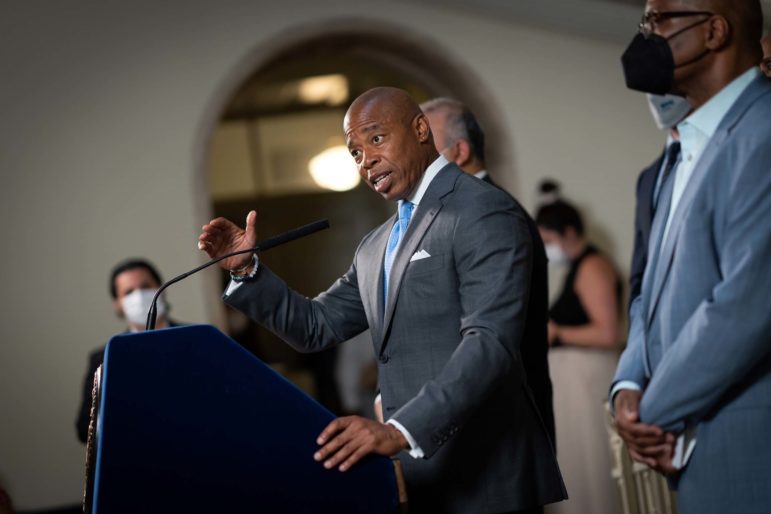 NYC Mayor Eric Adams talking into a microphone at a press conference podium