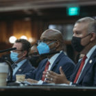 Three men at tables in NYC Council chambers